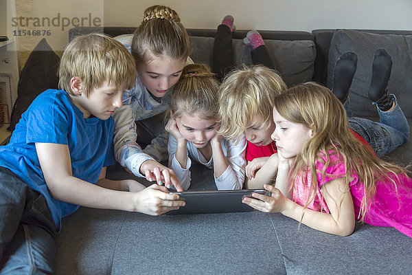 Fünf Kinder auf einer Couch mit digitalem Tablett zusammen