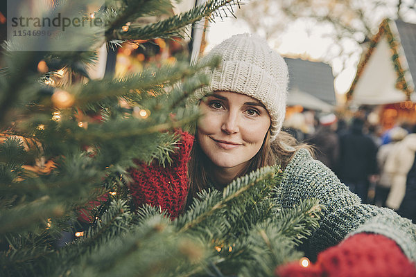 Frau schaut durch Koniferenzweige auf dem Weihnachtsmarkt