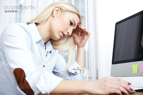 Überbeanspruchte blonde Frau am Schreibtisch sitzend