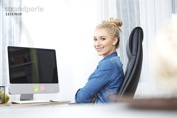 Porträt einer lächelnden blonden Frau am Schreibtisch in ihrem Büro