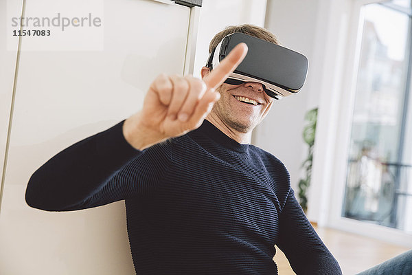Lächelnder Mann mit einer Virtual-Reality-Brille  die auf seinen Finger zeigt.