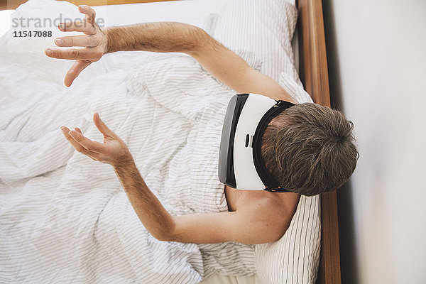Mann im Bett mit Virtual-Reality-Brille  der seine Hände bewegt