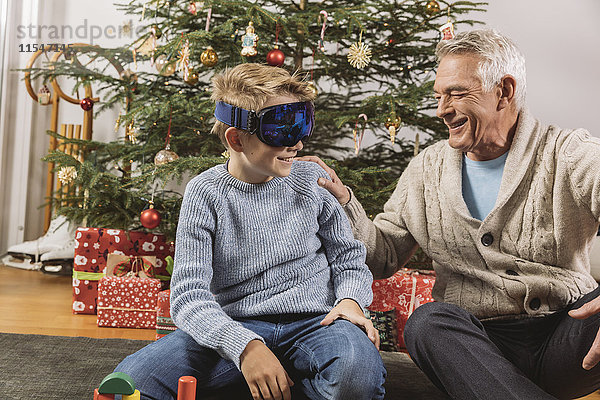 Glücklicher Großvater beim Anblick der neuen Skibrille des Enkels vor dem Weihnachtsbaum