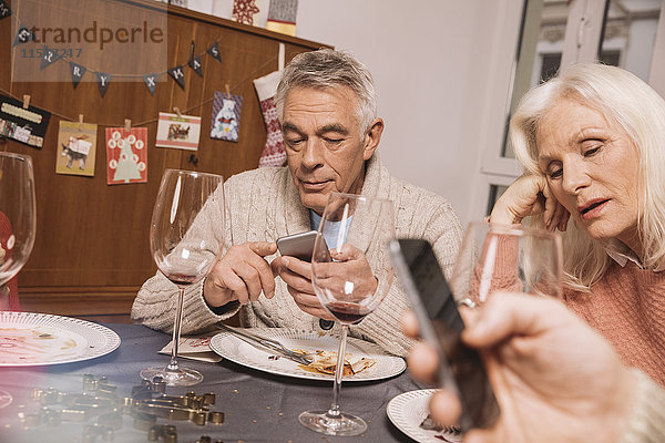 Verärgerte Seniorin mit Ehemann beim Smartphone nach dem Weihnachtsessen