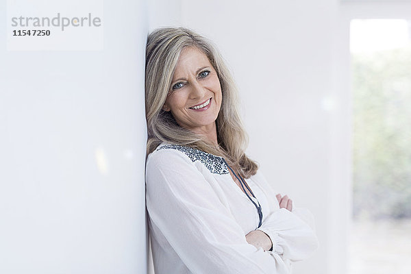 Porträt einer lächelnden  blonden Frau  die sich an die Wand lehnt.