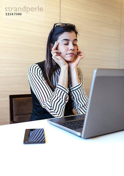 Porträt einer Geschäftsfrau mit geschlossenen Augen bei einer Pause am Schreibtisch