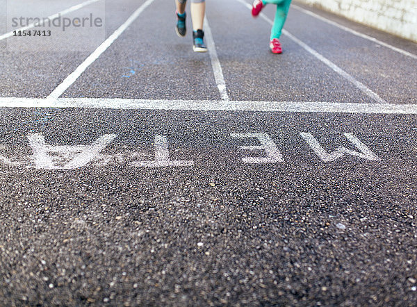 Beine zweier laufender Mädchen auf Asphalt