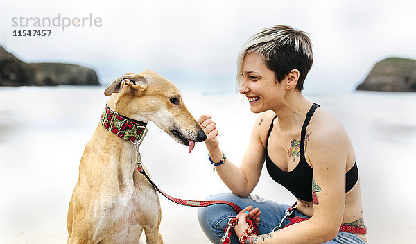 Spanien  Llanes  lächelnde junge Frau mit ihrem Windhund am Strand