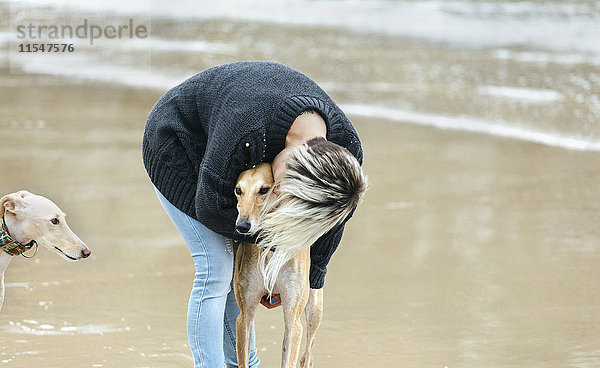 Spanien  Llanes  junge Frau küsst ihren Windhund am Strand