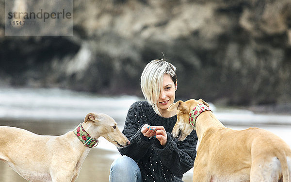 Spanien  Llanes  junge Frau füttert ihre Windhunde am Strand