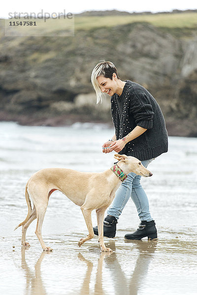 Spanien  Llanes  junge Frau spielt mit ihrem Windhund am Strand