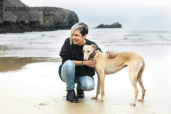 Spanien  Llanes  glückliche junge Frau mit ihrem Windhund am Strand