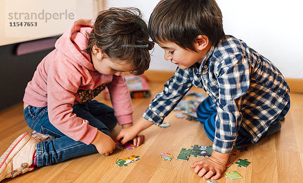 Junge und Mädchen machen zusammen ein Puzzle auf dem Boden.