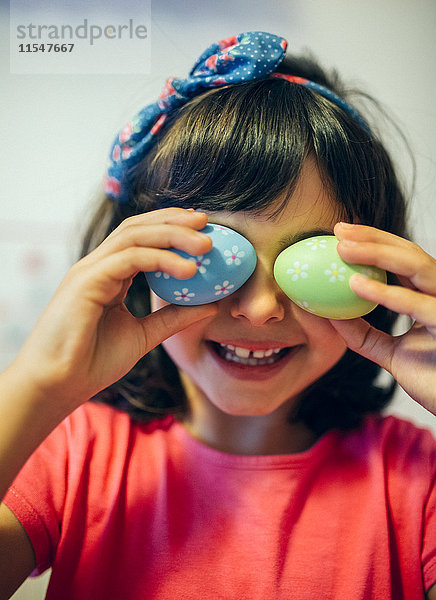 Kleines Mädchen bedeckt ihre Augen mit Ostereiern