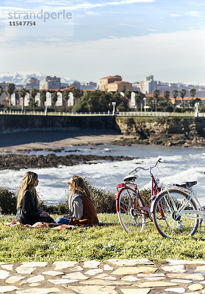 Zwei junge Frauen sitzen mit ihren Fahrrädern am Meer.