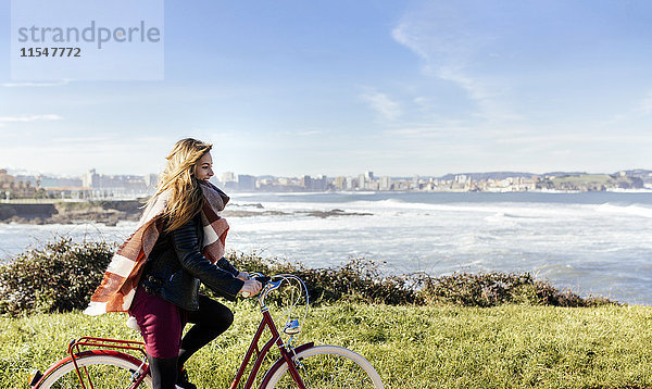 Spanien  Gijon  lächelnde junge Frau beim Radfahren an der Küste