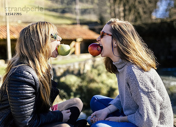 Zwei verspielte junge Frauen  die draußen Äpfel essen.