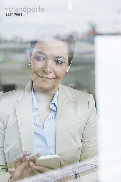 Geschäftsfrau mit Handy hinter der Fensterscheibe