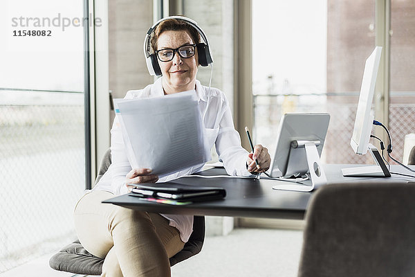 Geschäftsfrau mit Kopfhörer beim Lesen von Dokumenten im Büro