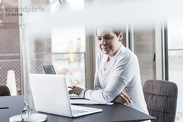 Lächelnde Geschäftsfrau am Schreibtisch mit Blick auf den Laptop