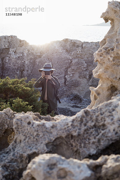 Spanien  Ibiza  Fotograf in Felsen stehend mit Diskettenhut beim Fotografieren