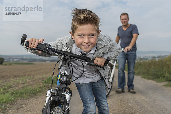 Portrait des kleinen Jungen auf Fahrradtour mit seinem Vater im Hintergrund