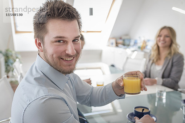 Lächelnder Mann mit einem Glas Orangensaft im Büro