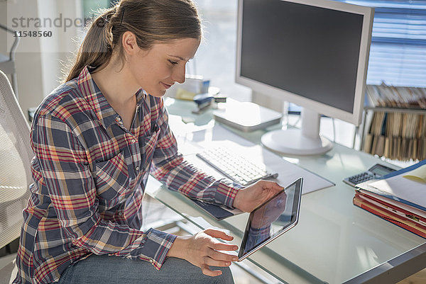 Junge Frau am Schreibtisch im Büro mit Blick auf das digitale Tablett