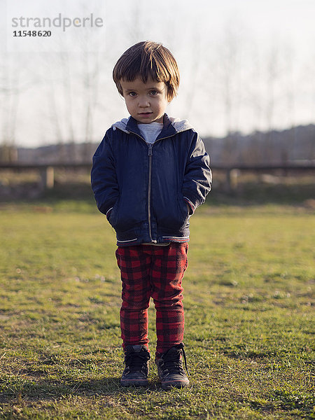 Kleiner Junge auf Gras stehend mit Händen in den Taschen