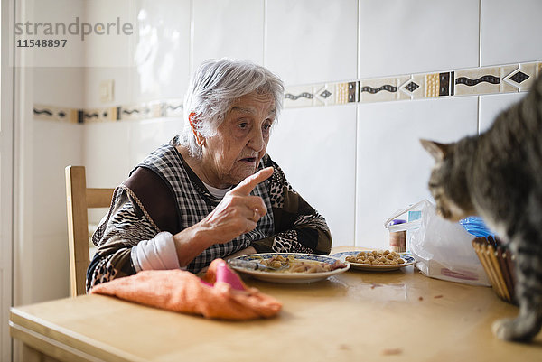 Seniorin sitzt am Esstisch und schimpft mit ihrer Katze.