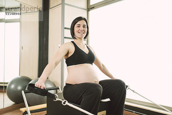 Schwangere Frau  die Pilates-Übungen mit einer Reformer-Pilates-Maschine in einem Fitnessstudio macht.