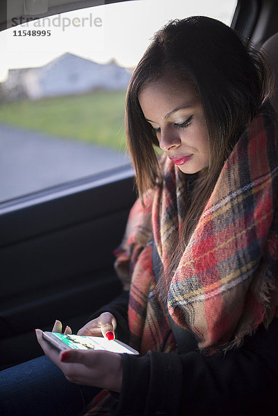 Spanien  Ferrol  Porträt einer jungen Frau  die in einem Auto sitzt und ihr Smartphone ansieht.