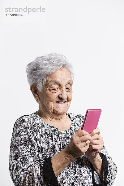 Porträt einer lächelnden Seniorin mit Blick auf ihr Smartphone vor weißem Hintergrund