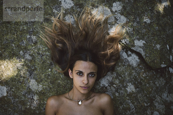 Porträt einer Frau  die auf einem Felsen mit zerzaustem Haar liegt.