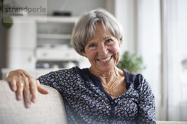 Porträt einer glücklichen Seniorin  die zu Hause auf der Couch sitzt.