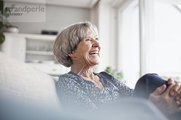 Porträt einer lachenden Seniorin  die zu Hause auf der Couch sitzt.