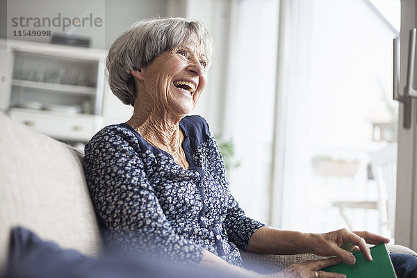 Porträt einer glücklichen Seniorin  die zu Hause auf der Couch sitzt.