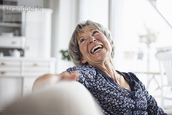 Porträt einer glücklichen Seniorin  die zu Hause auf der Couch sitzt.