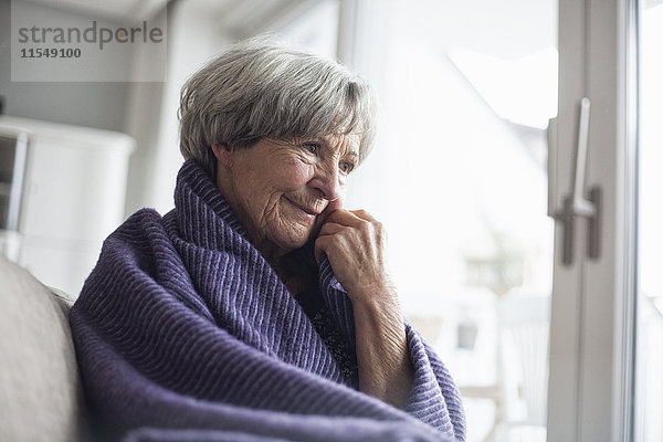 Porträt einer nachdenklichen Seniorin  die zu Hause auf der Couch sitzt.