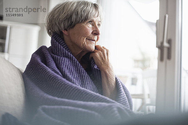 Porträt einer nachdenklichen Seniorin  die zu Hause auf der Couch sitzt.