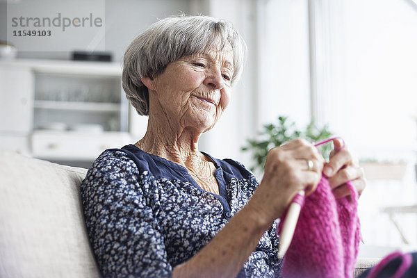 Porträt der strickenden Seniorin  die zu Hause auf der Couch sitzt.