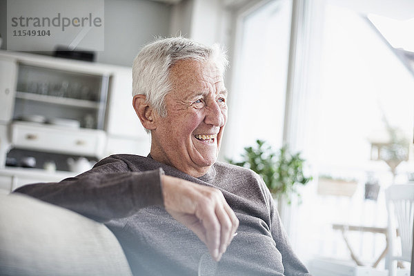 Porträt eines lachenden älteren Mannes  der zu Hause auf der Couch sitzt.
