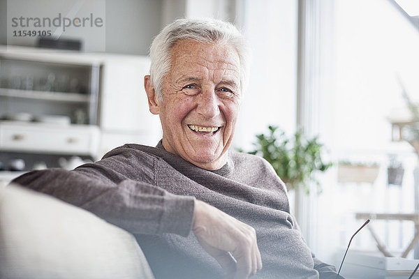 Porträt eines glücklichen älteren Mannes  der zu Hause auf der Couch sitzt.