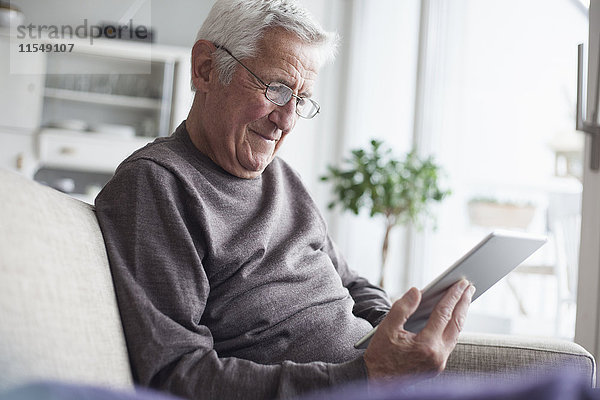 Porträt eines älteren Mannes  der zu Hause auf der Couch sitzt und ein digitales Tablett benutzt.