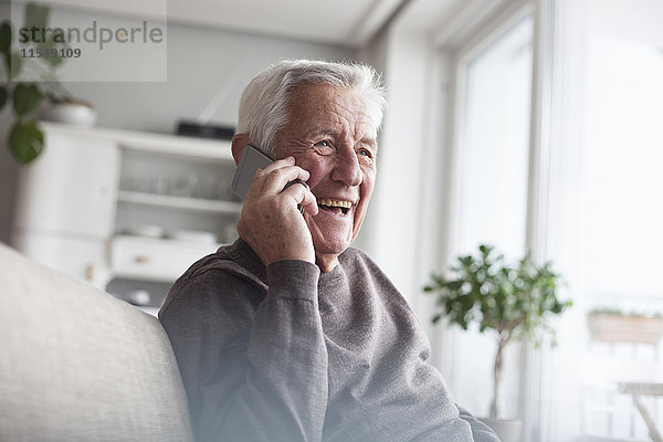 Porträt eines lachenden Senioren beim Telefonieren mit dem Smartphone zu Hause