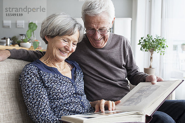 Glückliches älteres Paar  das auf der Couch des Wohnzimmers sitzt und sich ein Fotoalbum ansieht.