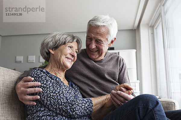 Fröhliches Seniorenpaar sitzt zusammen auf der Couch im Wohnzimmer