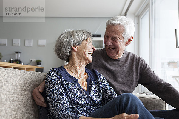 Lachendes Seniorenpaar  das zusammen auf der Couch im Wohnzimmer sitzt.