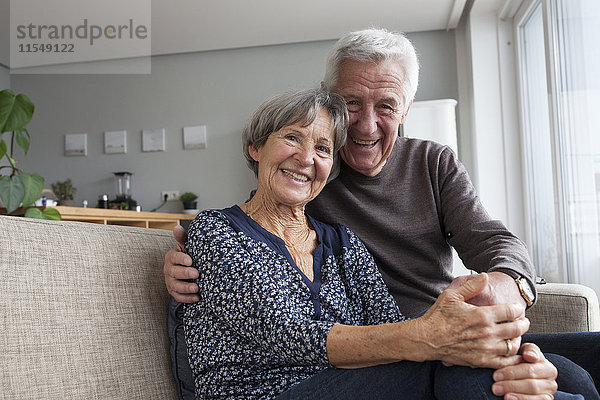 Glückliches älteres Paar  das auf der Couch im Wohnzimmer sitzt und Händchen hält.