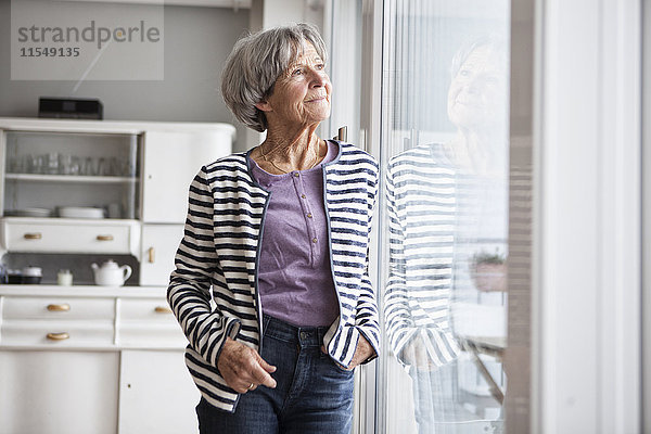 Porträt einer älteren Frau  die zu Hause durchs Fenster schaut.